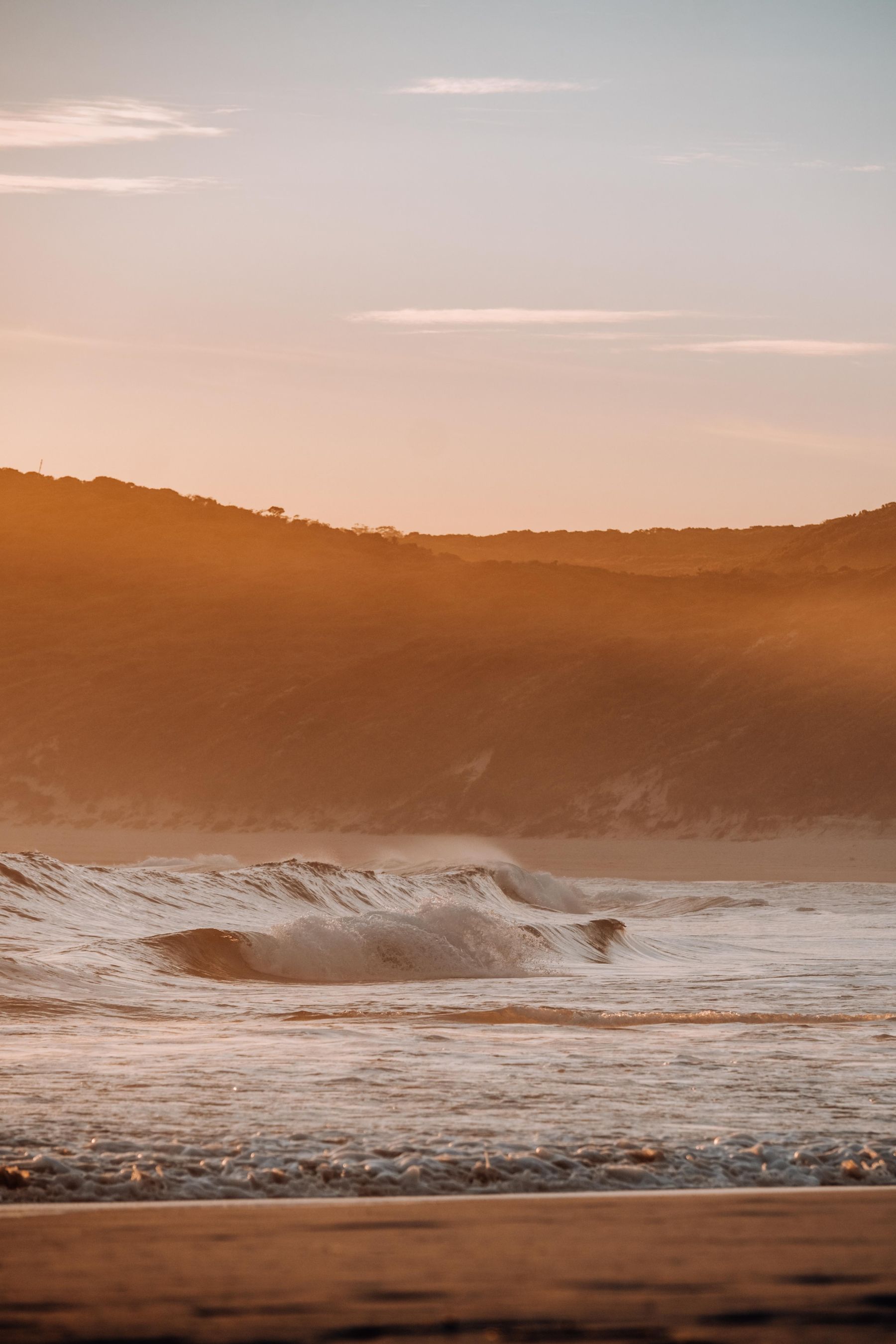 Waves breaking along a warm, empty shoreline at golden hour