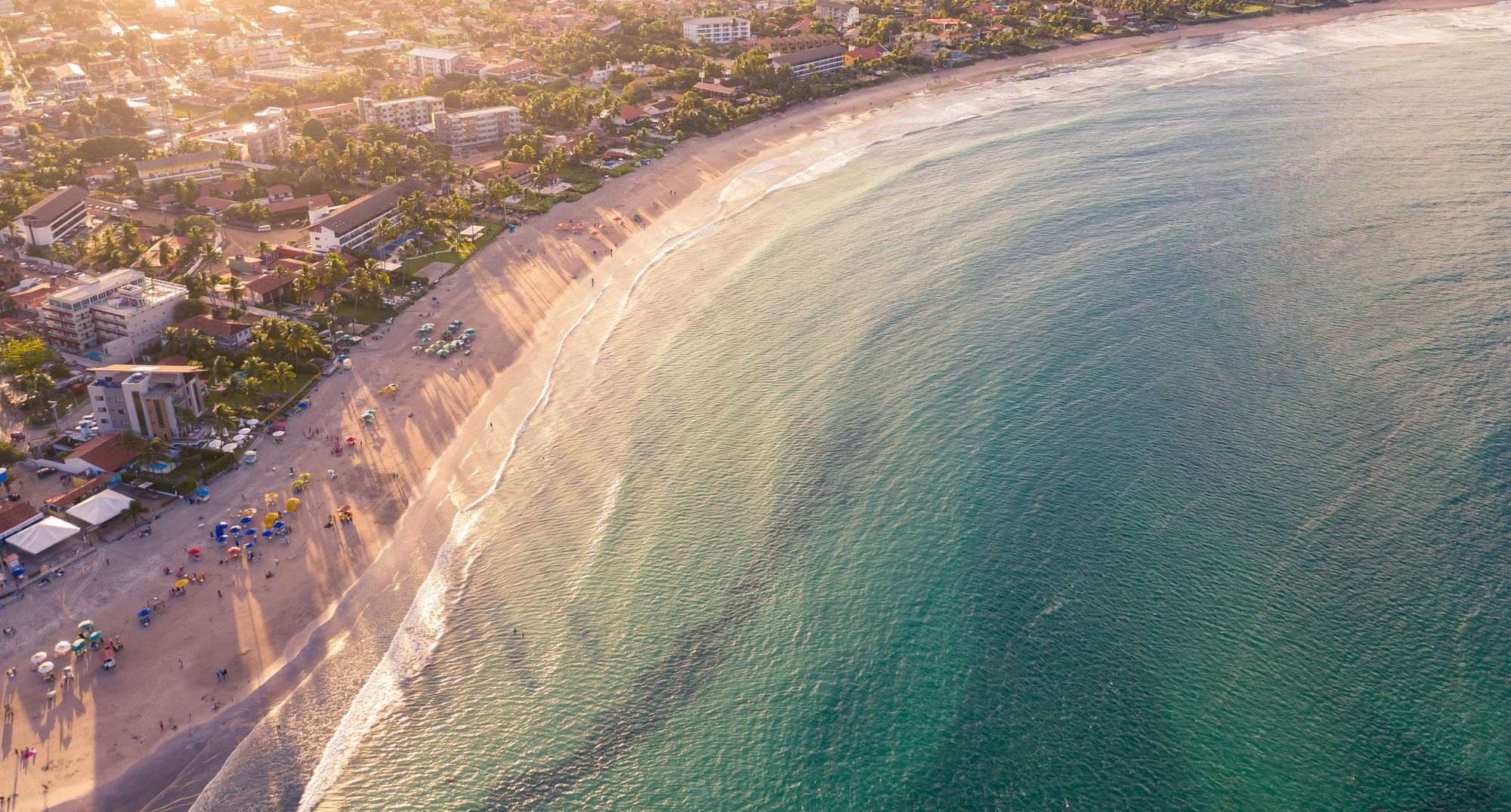 A wide beach town curving along turquoise water at golden hour