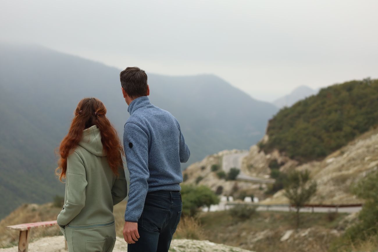 Two people in a hoodie and fleece looking out over misty mountains